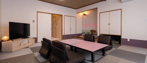 A room with a television, a dining table, and chairs. There are cabinets and a ceiling fan.