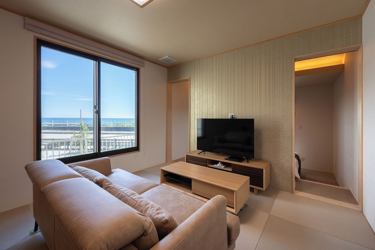 Een moderne woonkamer met een groot raam, een flatscreen televisie, een beige bank en een houten tv-meubel.
