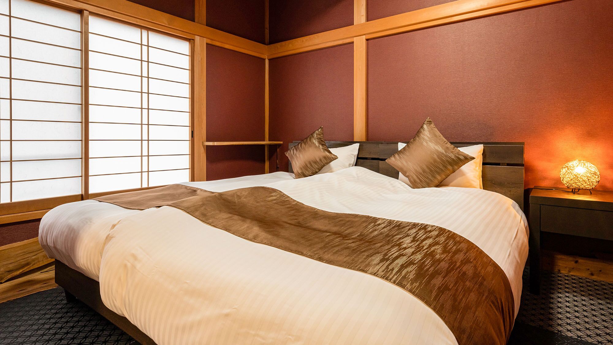 A hotel room with a bed, wooden headboard, and a nightstand with a lamp.