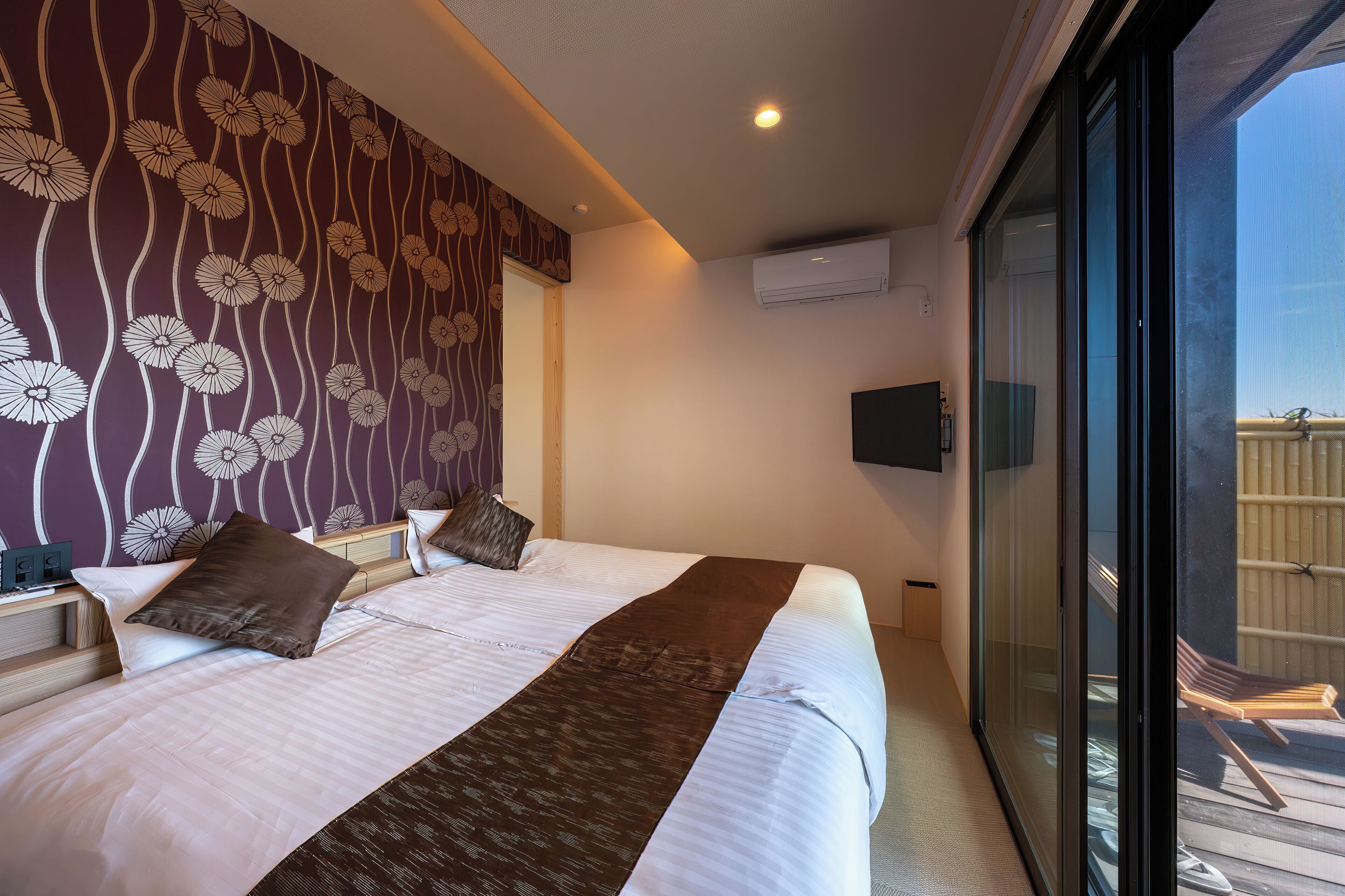 A hotel room with a large bed, a view of the outside balcony, and a patterned wall.
