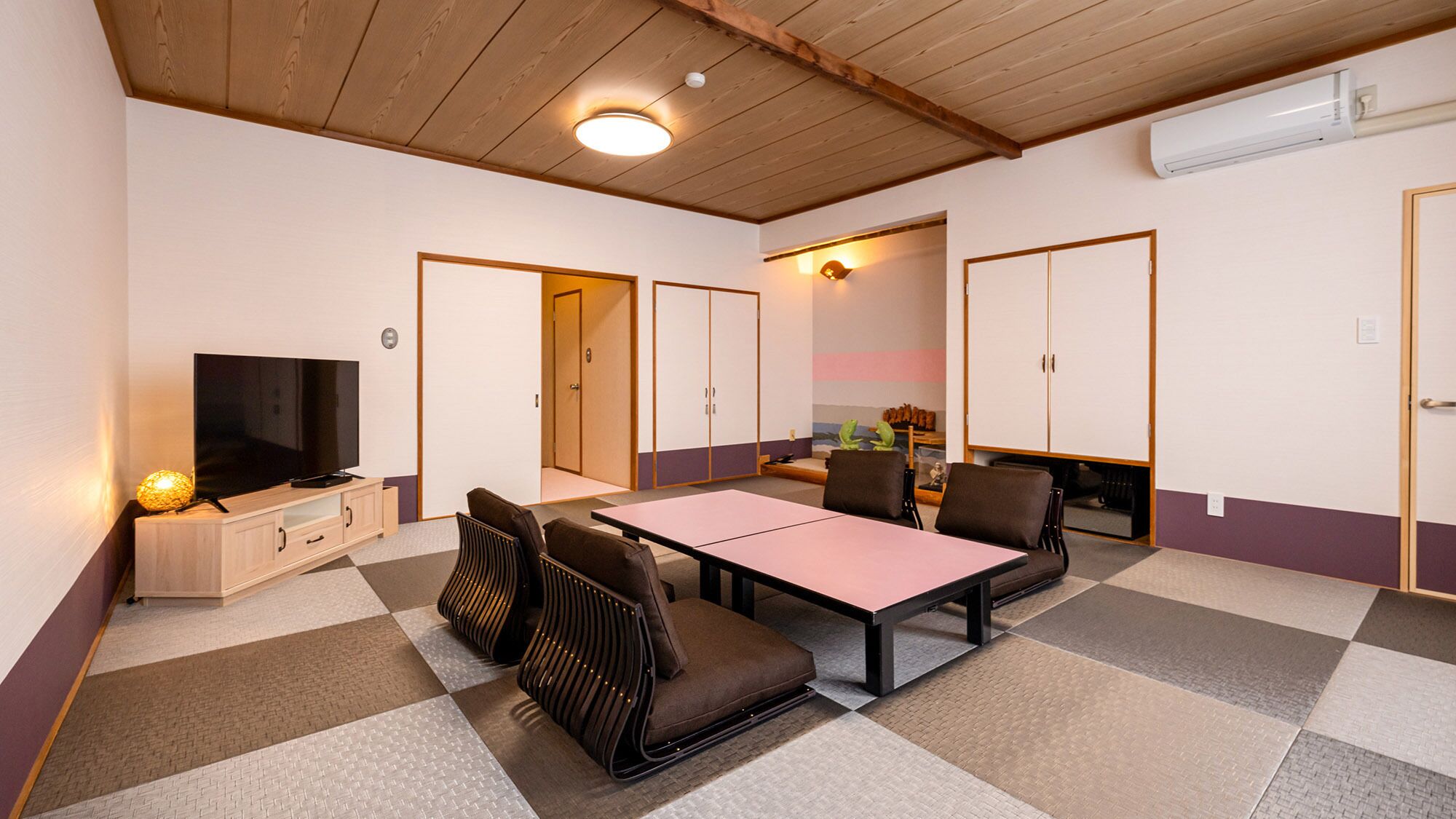 Una habitación con televisión, una mesa, sillas y un armario.