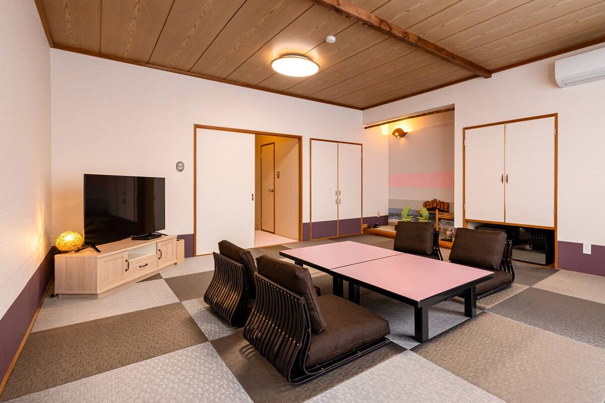 Una habitación con televisión, una mesa, sillas y un armario.