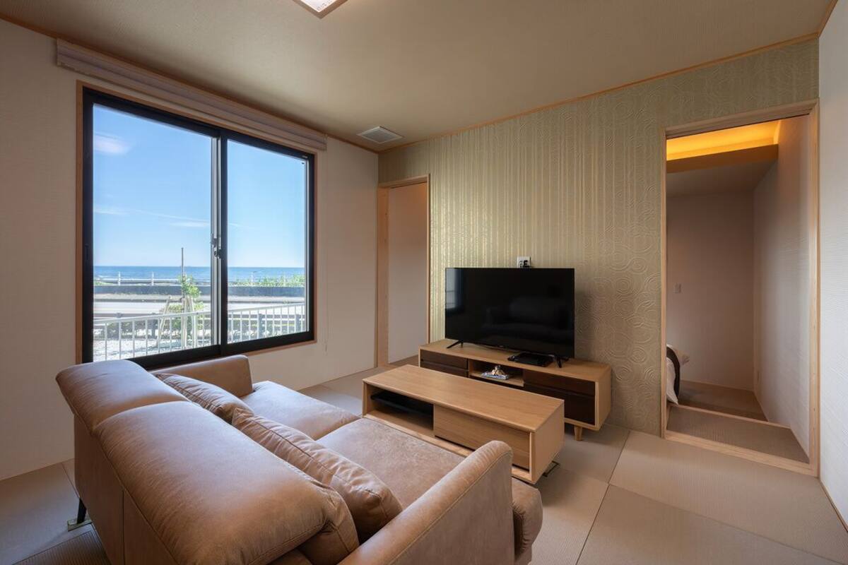 Una sala de estar moderna con un ventanal grande, un televisor de pantalla plana, un sofá beige y una mesa de centro de madera.