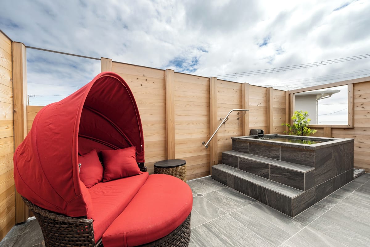 Een houten hut met een rode schommelstoel met kussens, een kleine hottub en een trap naar een hoger gelegen verdieping.