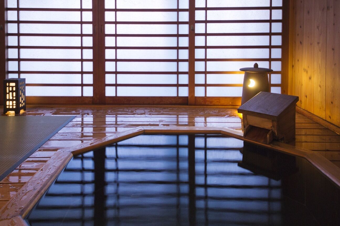 A traditional Japanese onsen with a wooden floor, a wooden bench, and a small lantern.
