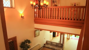 A two-story living area with a balcony, a chandelier, a sofa set, a coffee table, and a potted plant. - Hotel Ryuo Village (Yamanouchi)