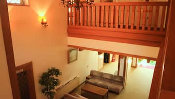 A two-story living area with a balcony, a chandelier, a sofa set, a coffee table, and a potted plant.