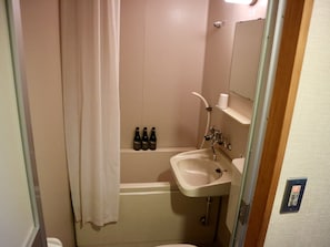 A bathroom with a bathtub, a sink, and a toilet. There are four bottles on the shelf above the bathtub.
