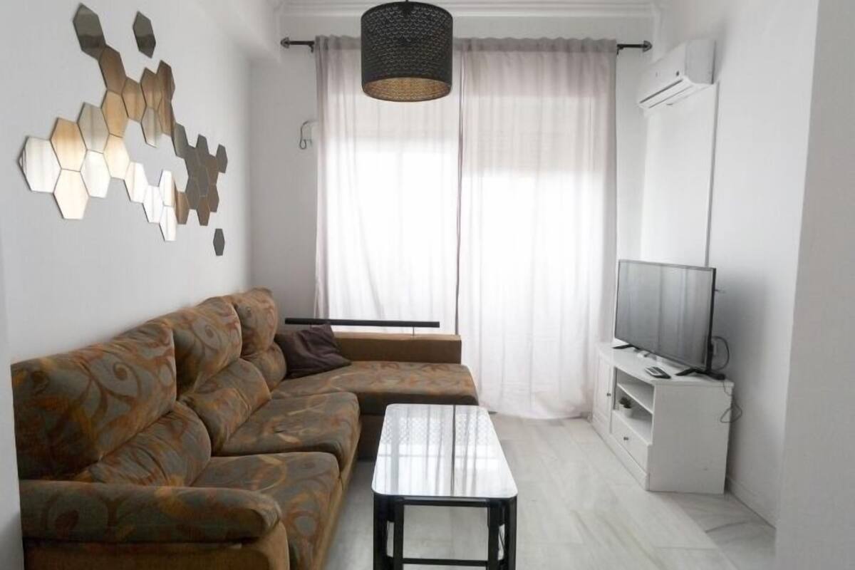 Un salon moderne avec un canapé d’angle, une table basse, un téléviseur posé sur un meuble et un élément décoratif mural.