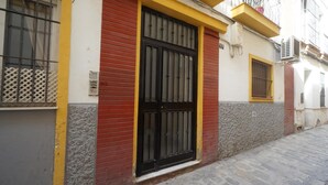 Un edificio con una gran verja negra, paredes rojas y amarillas, y un ventanal pequeño con barrotes.
