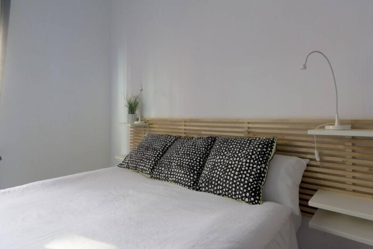 Une chambre à coucher moderne avec une tête de lit en bois, une couvre-lit blanche et une table de chevet avec une lampe.