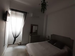 A bedroom with a bed, a dresser, a mirror, and a hanging plant.