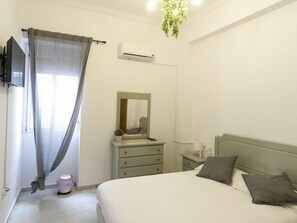 A bedroom with a bed, a dresser, a mirror, a toilet, and a TV. - RentalSevilla Apartamento recién reformado en el Gran Poder (Seville)