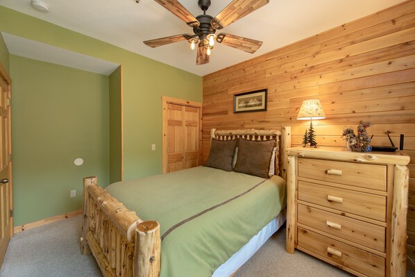 Un dormitorio con una cama de madera, una mesita de noche con cajones, un ventilador de techo y una lámpara.