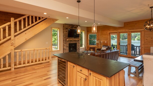 A spacious kitchen with a central island, wooden staircase, and a stone fireplace. - Dog Friendly Townhome w/ Deck & Sunset Views (McHenry)