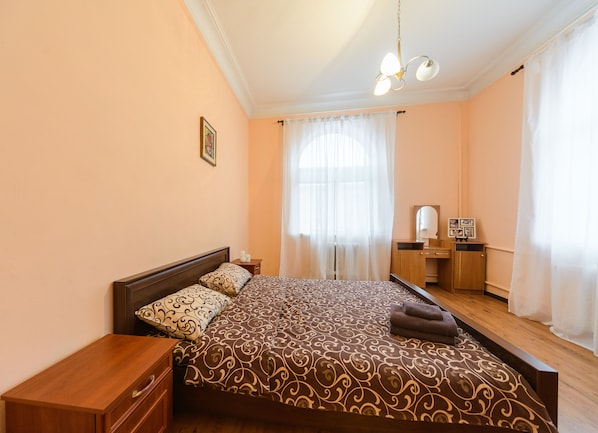 A bedroom with a large bed, a wooden nightstand, a dresser, and a mirror.
