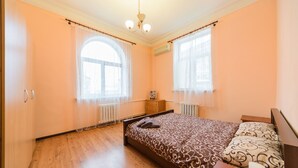 Una camera da letto con pavimento in legno, un letto con copriletto decorato, un comodino e una cassettiera.