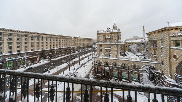 Paesaggio urbano innevato con edifici storici e un monumento centrale.
