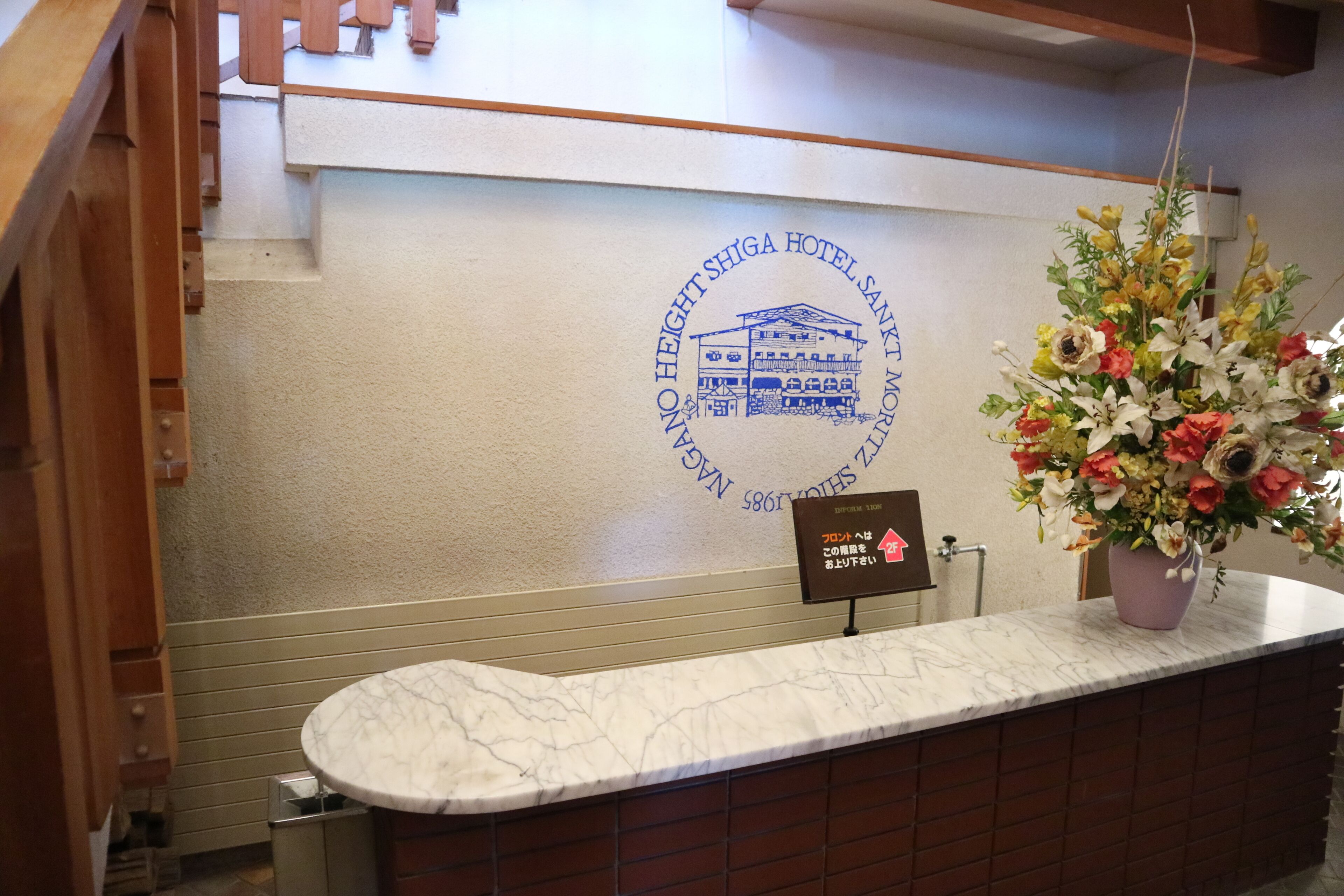 A reception desk with a marble top, a logo on the wall, and a flower arrangement.