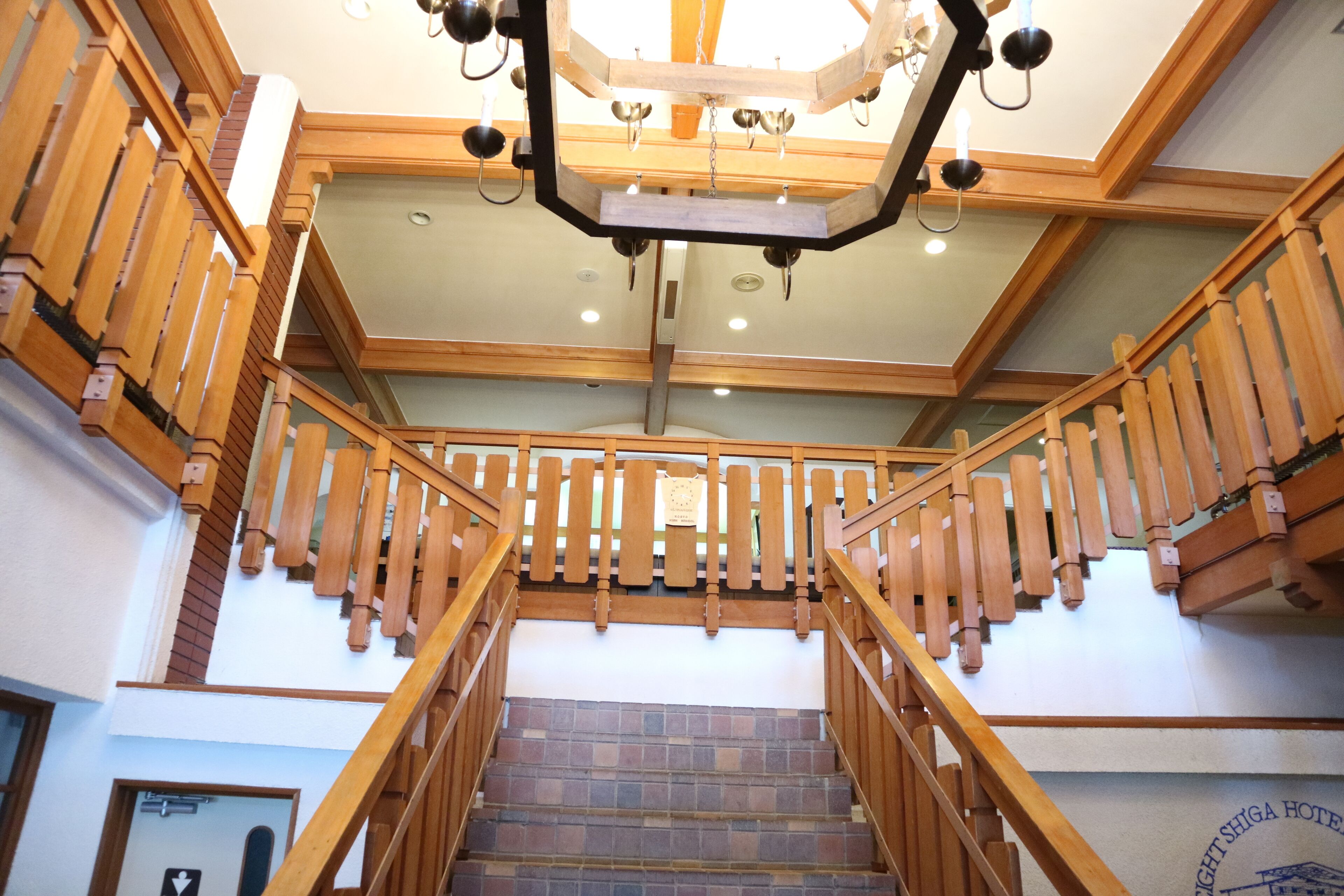 Una escalera de madera con un candelabro, un cartel que indica el nombre del hotel y vista del interior.