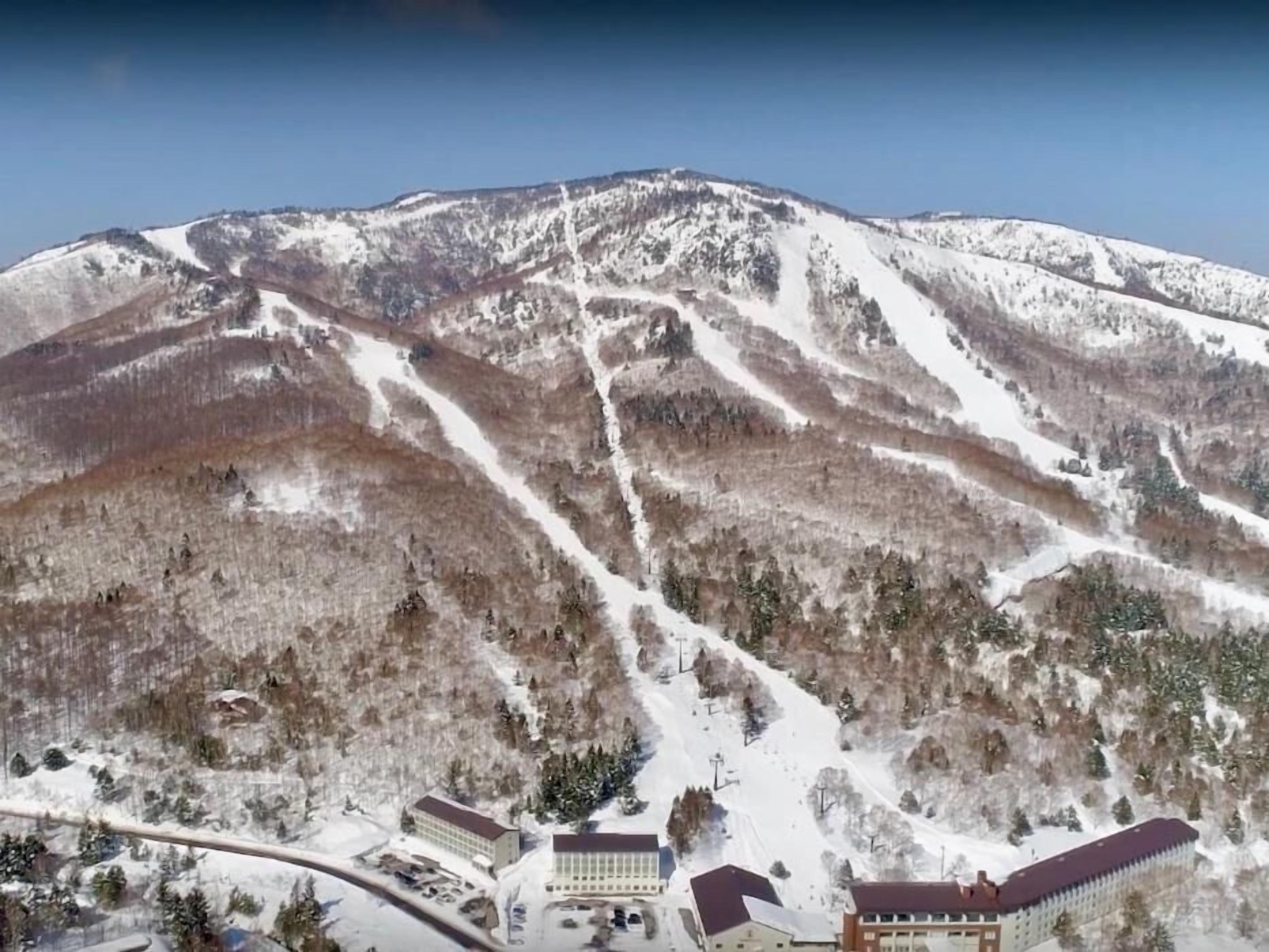 Une montagne enneigée, dotée de pistes de ski et d’une zone de station avec des bâtiments et un parking.