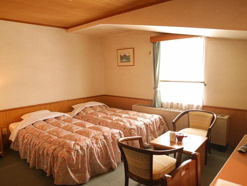A hotel room with two beds, a desk, and a chair.