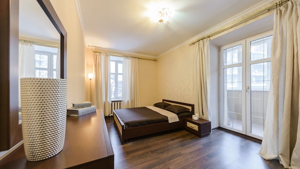A bedroom with a bed, bedside table, lamp, and a large window with curtains. - Apartments Kreshchatik 17-21 (Kyiv)