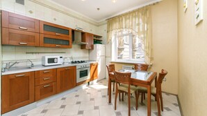 A kitchen with wooden cabinets, a microwave, a stove, and a dining table with chairs. - Apartments Kreshchatik 17-39 (Kyiv)
