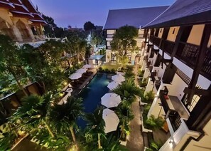 A pool area with lounge chairs and umbrellas, surrounded by lush greenery and traditional architecture. - Aksara Heritage (Chiang Mai)