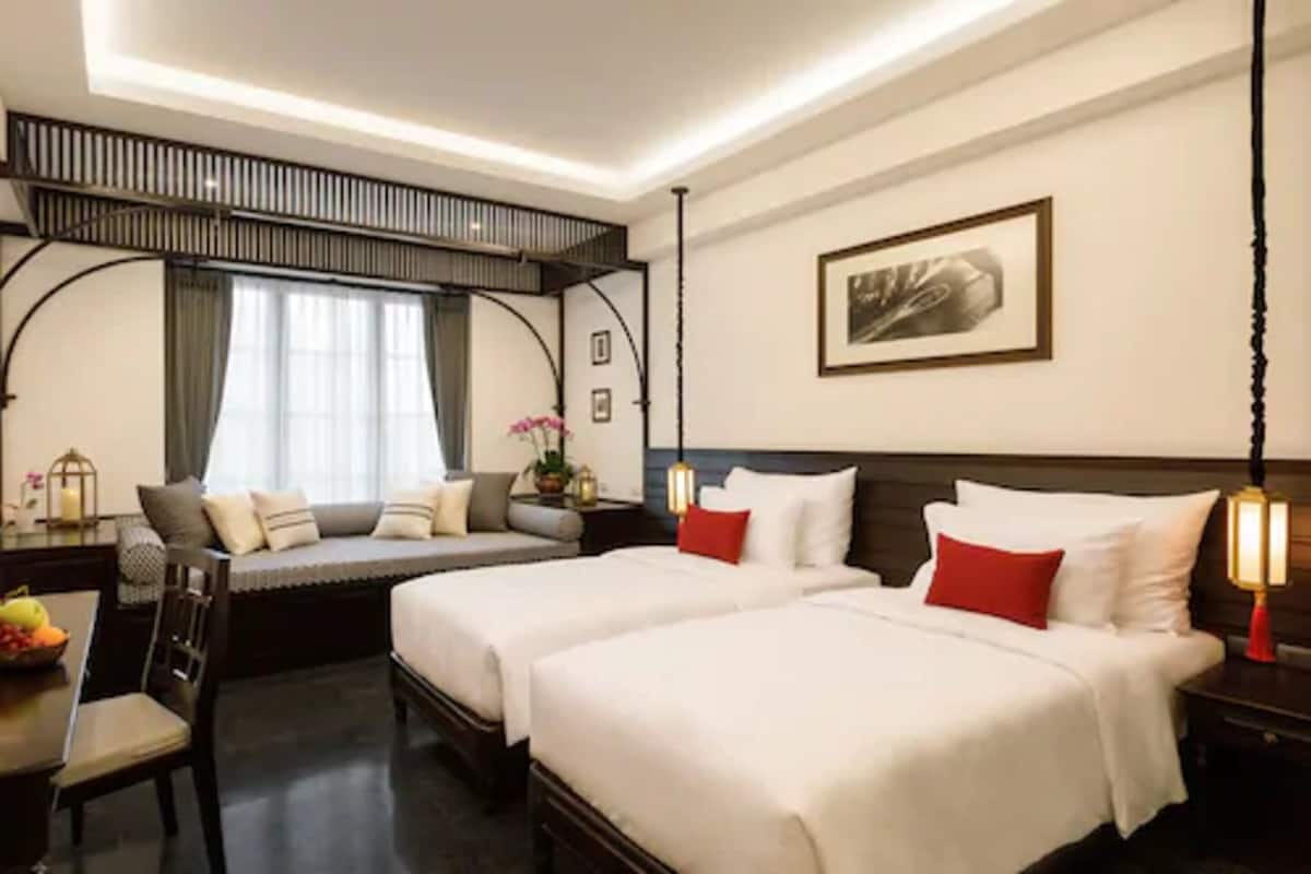 Habitación de hotel con dos camas, zona de estar, mesa de comedor y un ventanal grande.