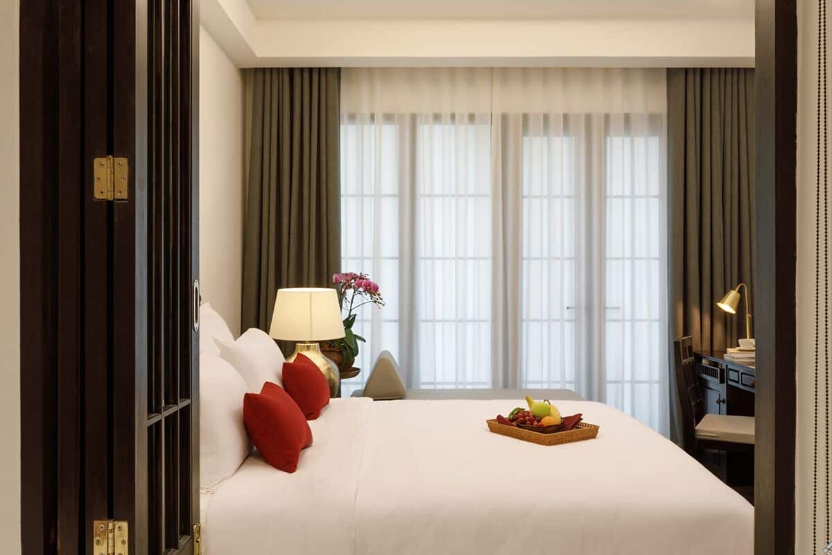 Una habitación de hotel con una cama grande, un escritorio, una lámpara y una ventana con cortinas.