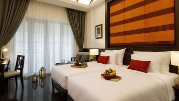 A hotel room with two beds, a desk, a chair, a lamp, and a large decorative wall panel.
