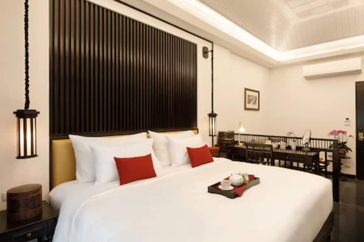 Una habitación de hotel con una cama grande, cabecera de madera, lámparas de noche, mesita de noche y bandeja con tetera y taza.