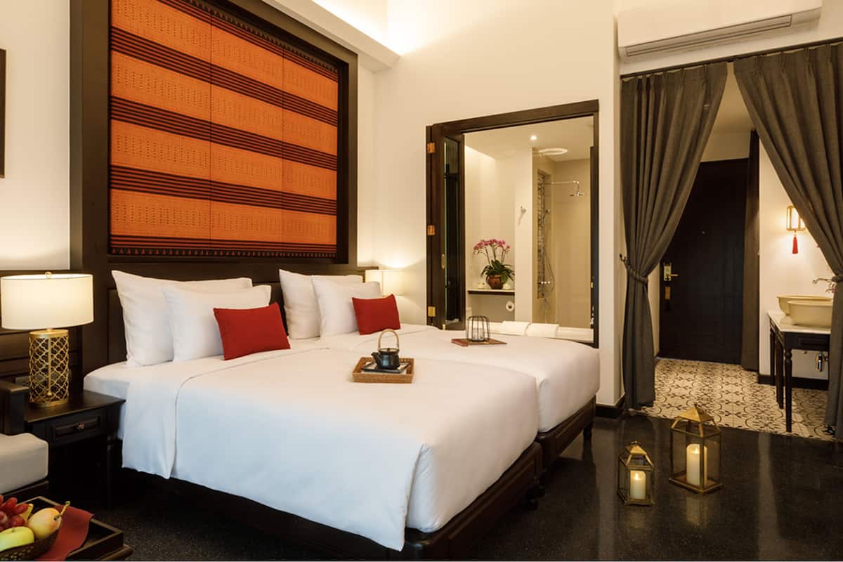 Habitación de hotel con una cama grande, mesitas de noche, un espejo, un baño visible a través de una puerta abierta y un frutero en el suelo.