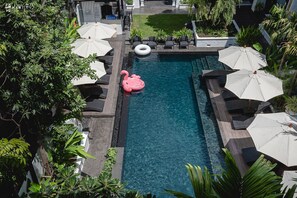 A swimming pool with lounge chairs and umbrellas, surrounded by greenery. - Aksara Heritage (Chiang Mai)