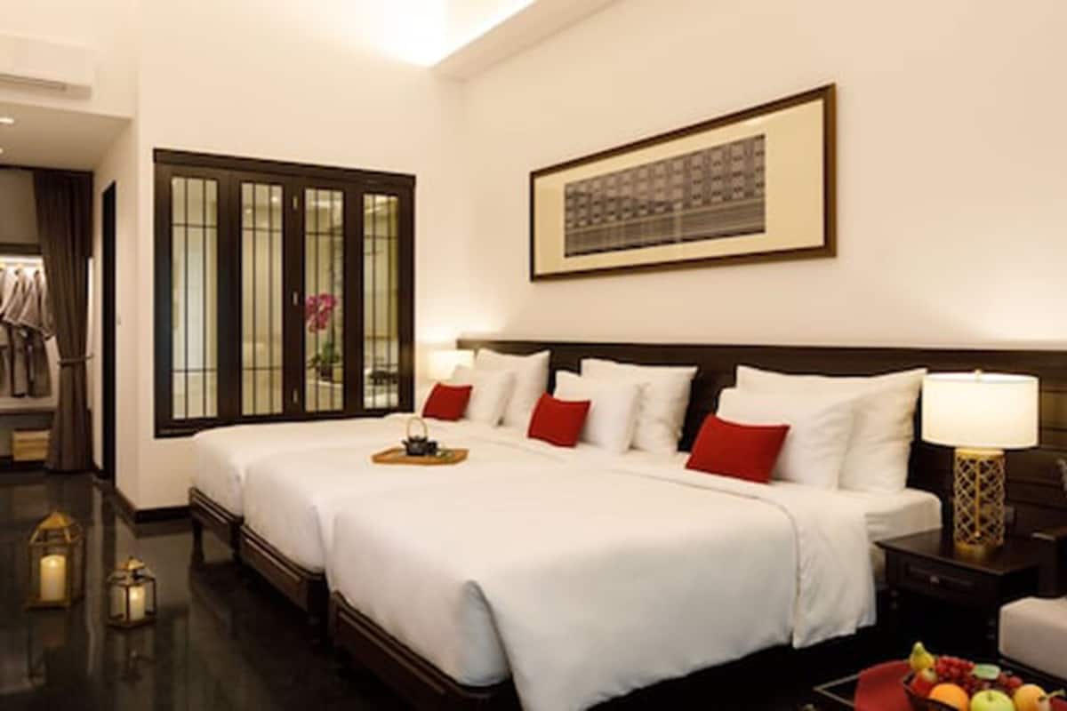 Habitación de hotel con una cama grande, una mesita de noche con lámpara, un cuadro en la pared y una ventana con cortinas.