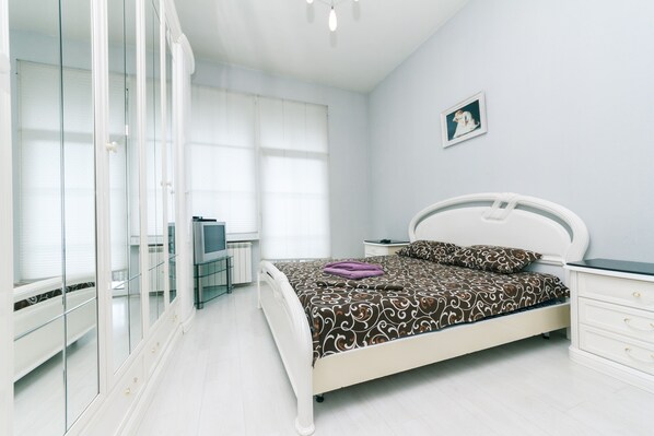 A bedroom with a bed, a nightstand, a dresser, a TV, and a wardrobe.