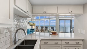 Une cuisine moderne avec des meubles blancs, une grande fenêtre donnant sur la mer et un coin repas avec une table et des chaises.