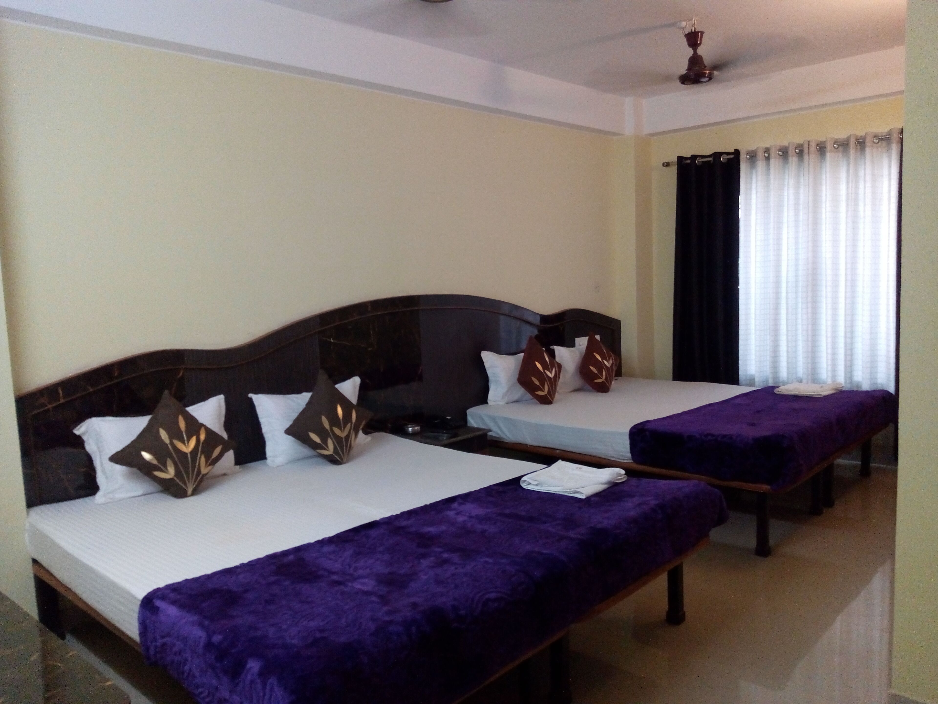 Une chambre d’hôtel avec deux lits, chacun recouvert d’une couvre-lit violette et agrémenté de coussins décoratifs.