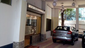 A covered parking area with a car parked inside, a tiled floor, and a door leading to a building. - Hotel Niladrii Galaxy (Siliguri)
