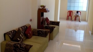 A spacious living area with a sofa set, a wooden side table, and a red chair. - Hotel Niladrii Galaxy (Siliguri)