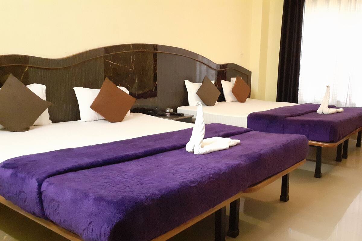 Habitación de hotel con dos camas, cada una con cubrecama morado y almohadas blancas. Hay una mesita de noche con una lámpara entre las camas.