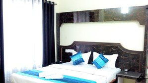 A neatly made bed with a blue and white bedspread, a wooden headboard, and a nightstand with a lamp. - Hotel Niladrii Galaxy (Siliguri)