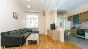 A modern living room with a sectional sofa, a wooden coffee table, and a TV on a wooden cabinet. The kitchen features wooden cabinets, a microwave, and a stove. - Apartments Kreshchatik 27-47 (Kyiv)
