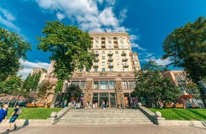 A large, historic building with multiple floors, a central entrance with steps, and surrounding trees. - Apartments Kreshchatik 27-47 (Kyiv)
