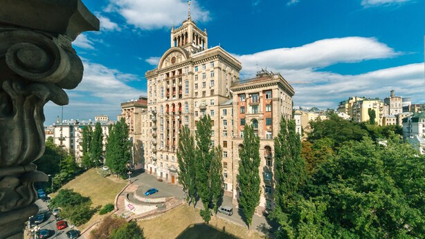A large, historic building with multiple floors and a prominent tower, surrounded by trees and other buildings. - Apartments Kreshchatik 27-47 (Kyiv)