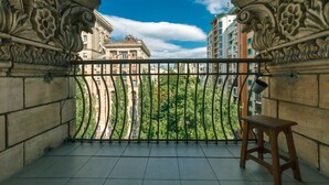 A balcony with ornate metal railings, a wooden stool, and a view of buildings and trees. - Apartments Kreshchatik 27-47 (Kyiv)