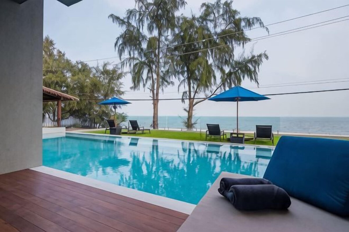 Piscina con sillones de descanso y sombrillas, con vista al mar.