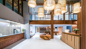 A spacious lobby with a central wooden reception desk, high ceilings, and hanging wicker chandeliers. - Lullaby The Sea Hua Hin (Cha-am)