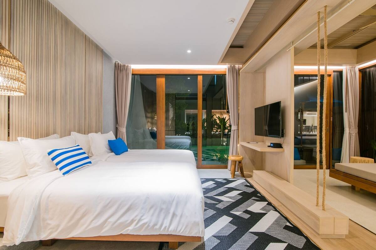 Una habitación de hotel moderna con una cama grande, televisión y balcón con cortinas.
